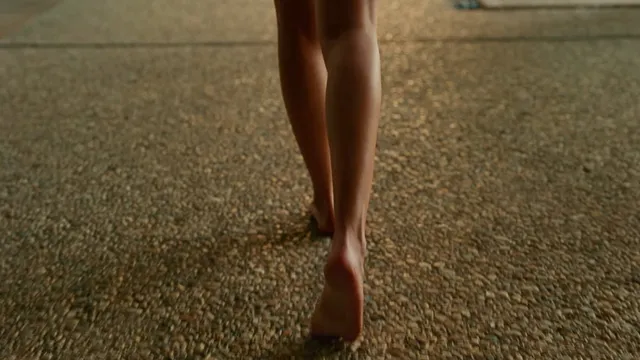 Dakota Johnson standing barefoot on a rug.