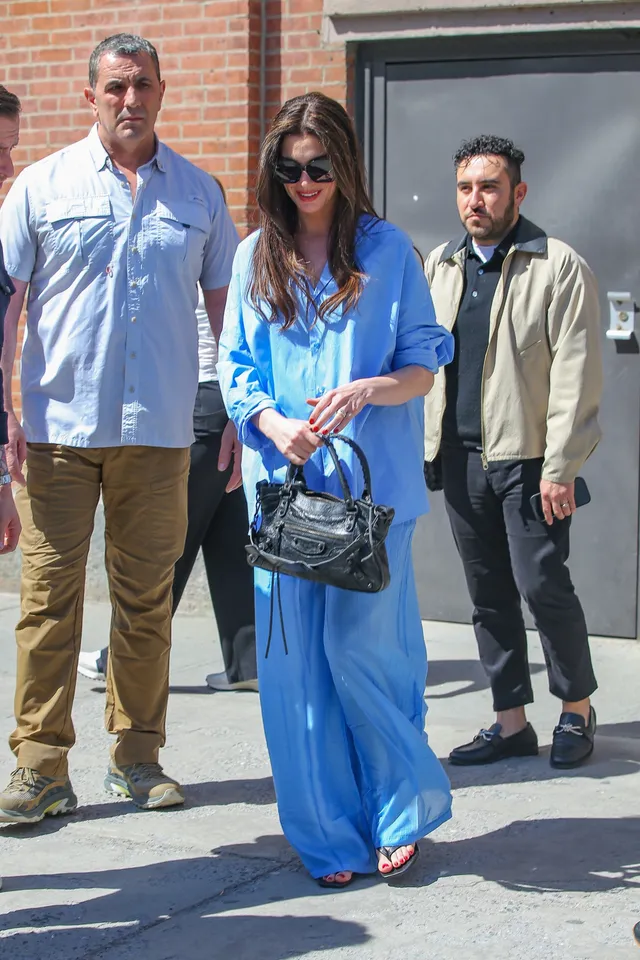 Anne Hathaway walking outside in a blue dress and open-toe heels.