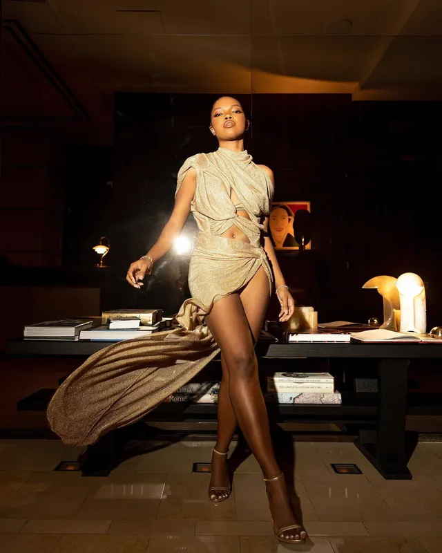Ryan Destiny posing in a flowing gold dress and metallic heels.
