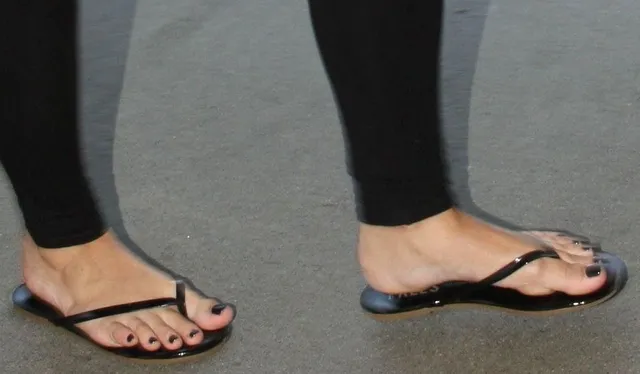 Demi Lovato wearing black flip-flops beneath dark leggings.