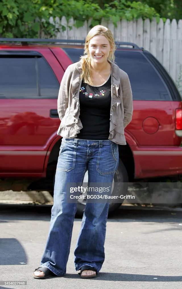 Kate Winslet standing outdoors in jeans and sandals.