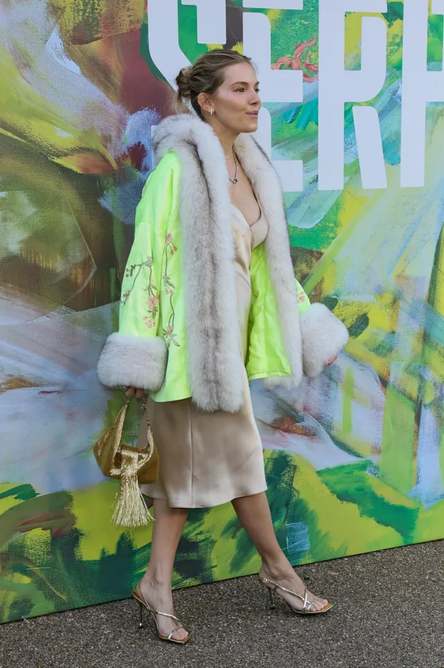 Sienna Miller posing in a pale dress and bright coat.