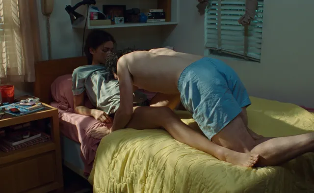Zendaya resting bare feet on a bed in a film scene.