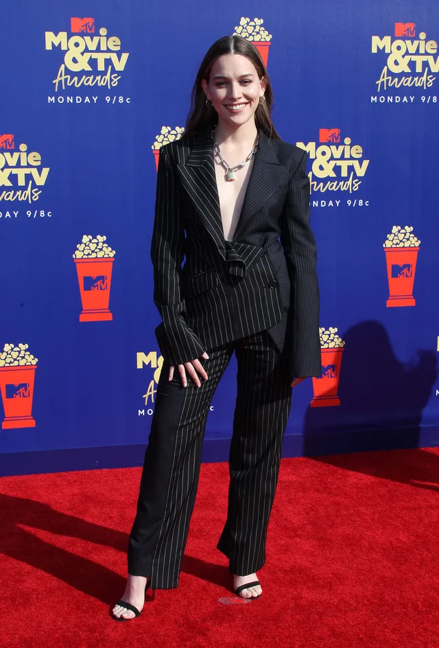 Victoria Pedretti posing at an awards event in a dark suit.