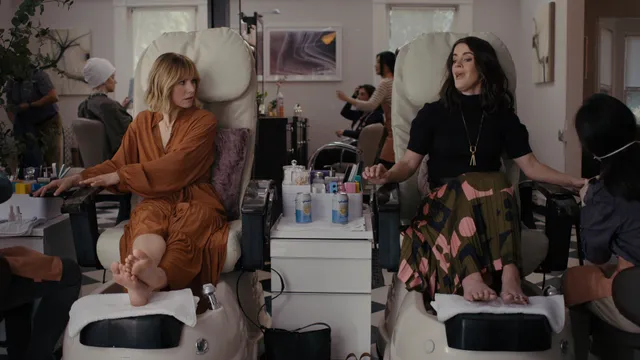 Kristen Bell sitting barefoot at a pedicure station beside another person.