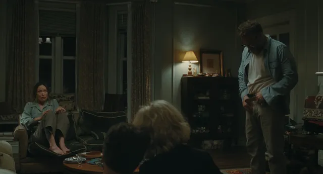 Olivia Wilde sitting indoors beside other people in a dimly lit film scene.