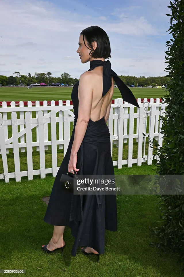 Hayley Atwell turning beside a white fence in a halter dress.