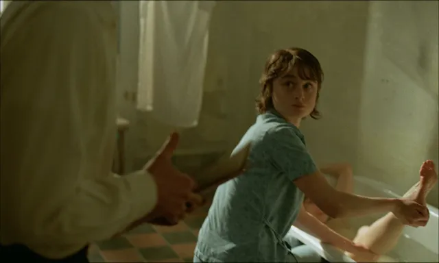 Felicity Jones sitting in a bathtub in a screen scene.