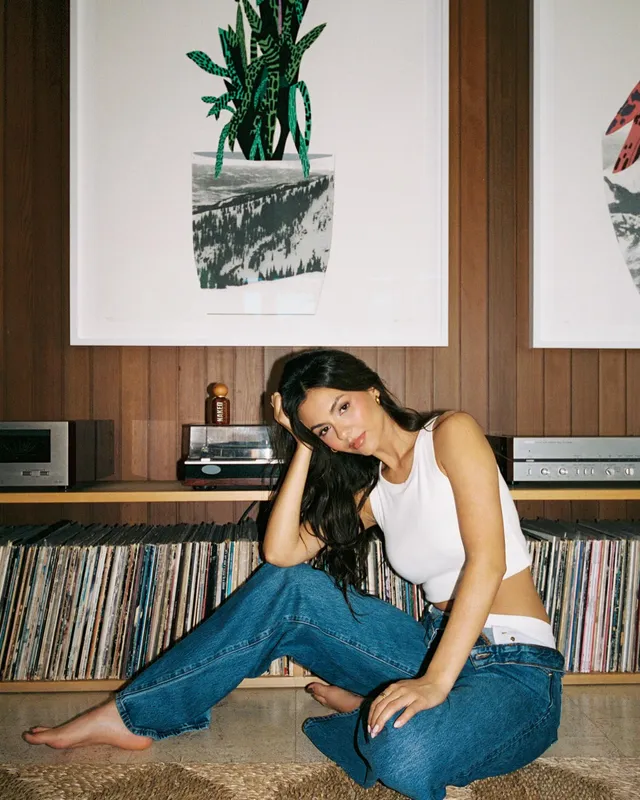 Victoria Justice sitting barefoot in jeans beside record shelves.