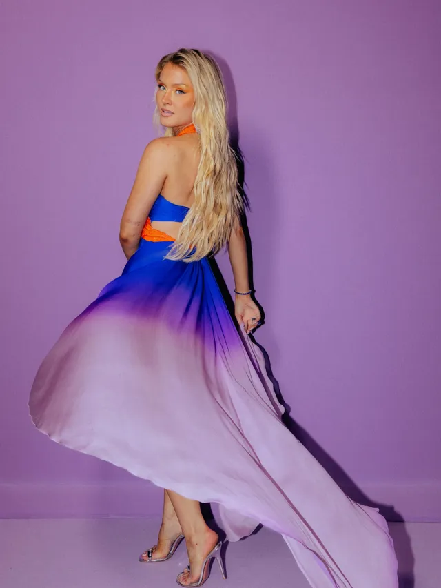 Zara Larsson posing in a flowing purple dress and purple heels.