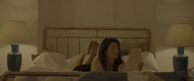 Gemma Arterton sitting against pillows in a bedroom scene.