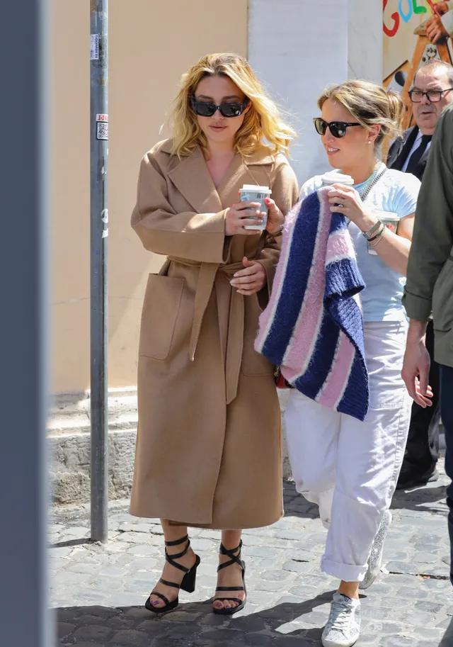 Florence Pugh walking in a tan coat and black heels.