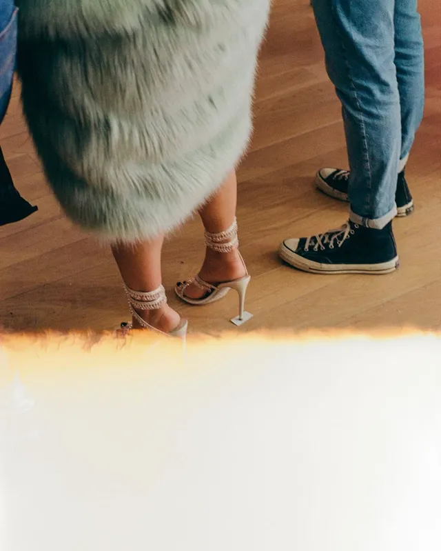 Naomi Scott showing pale heels beneath a textured skirt in a film scene.
