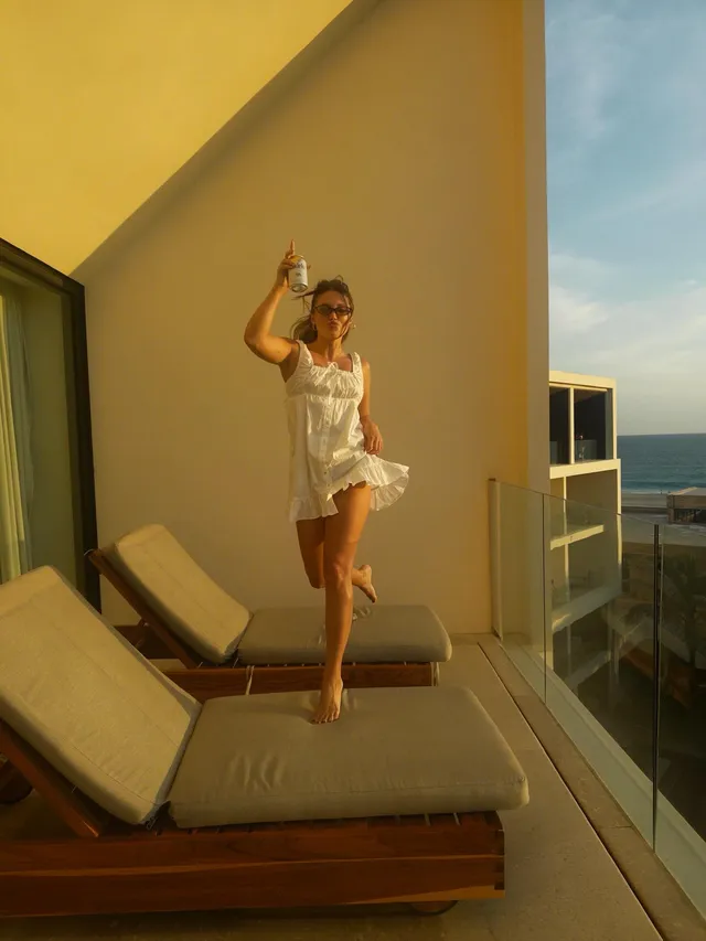 Olivia Holt standing barefoot on an outdoor lounger in a white outfit.