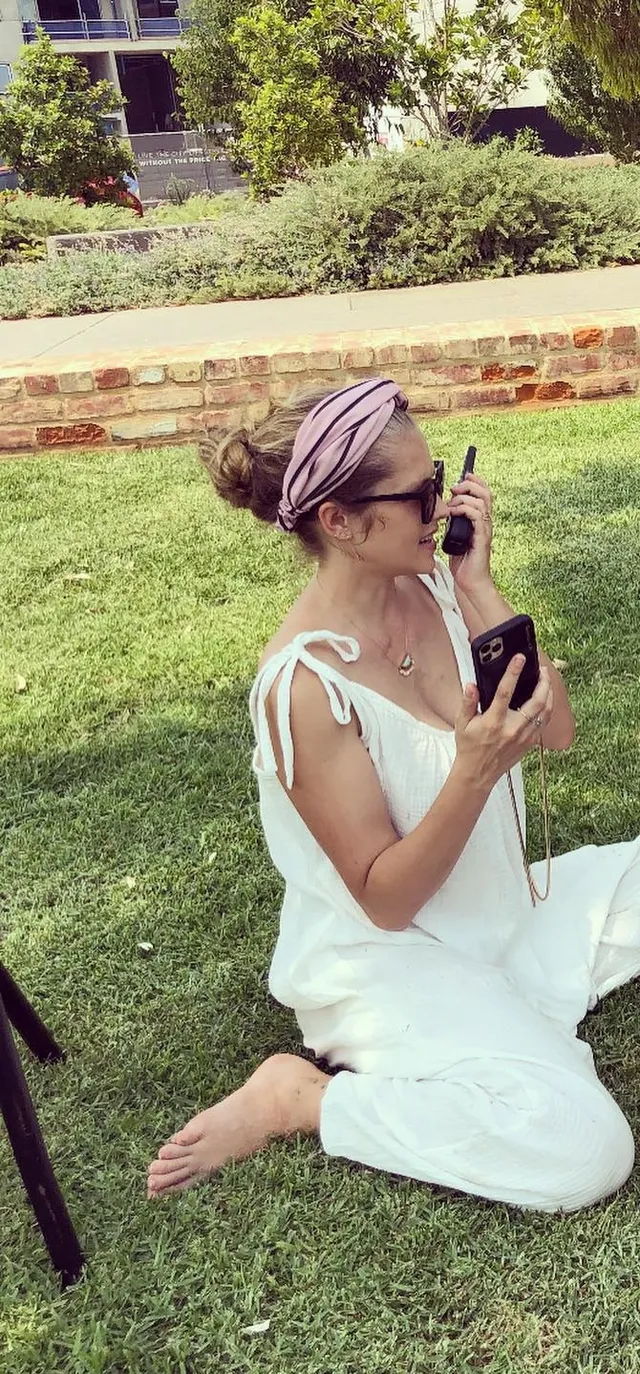 Teresa Palmer sitting on grass in a white outfit.