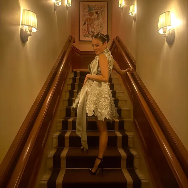 Chase Sui Wonders posing on stairs in a silver dress and black heels.