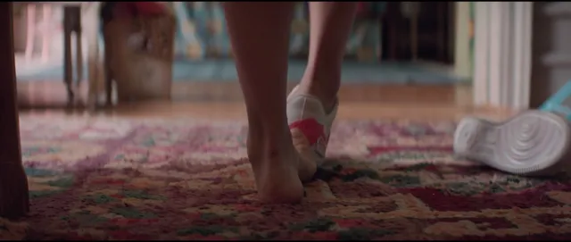 Melissa Barrera walking barefoot across a rug beside discarded shoes.