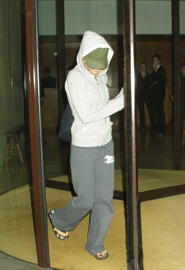Avril Lavigne walking through a doorway in a tracksuit and open-toe footwear.