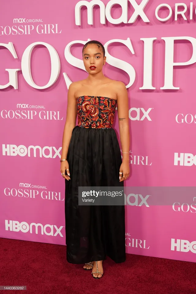Whitney Peak posing in an embellished top, black skirt and gold heels on a red carpet.