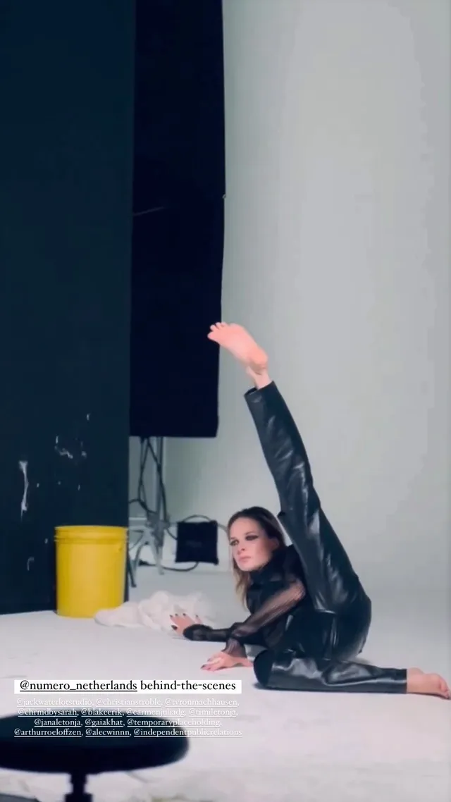 Rebecca Ferguson stretching barefoot on a studio floor in a dark outfit.