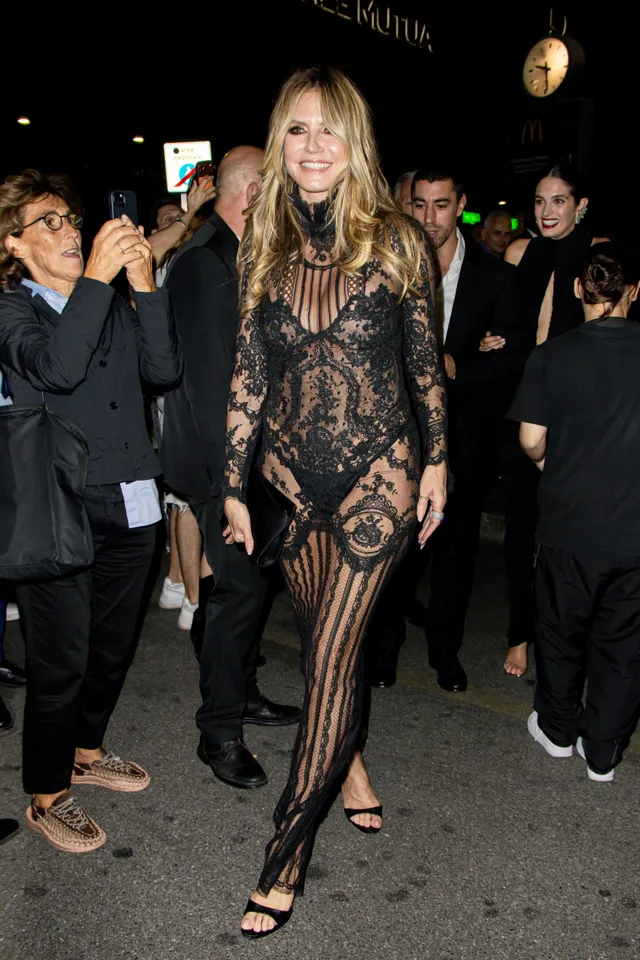 Heidi Klum walking among guests in a long black lace gown and heels.