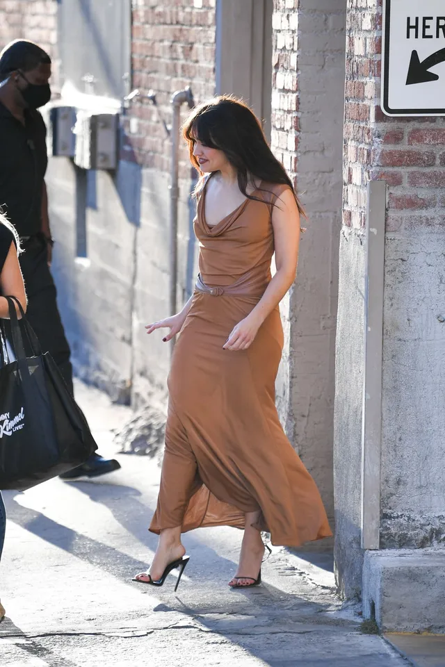 Olivia Cooke walking outside in a brown dress and pointed pumps.