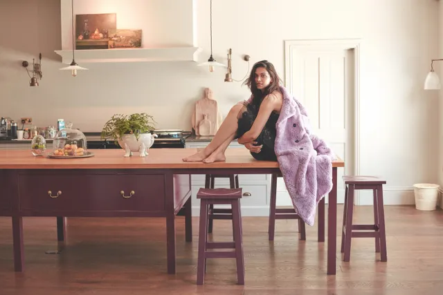 Deepika Padukone sitting barefoot on a kitchen counter in a pale patterned dress.