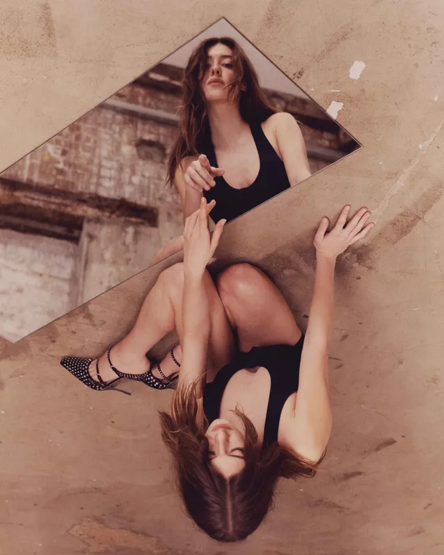Daisy Edgar-Jones posing with a mirrored surface in a black dress and heels.