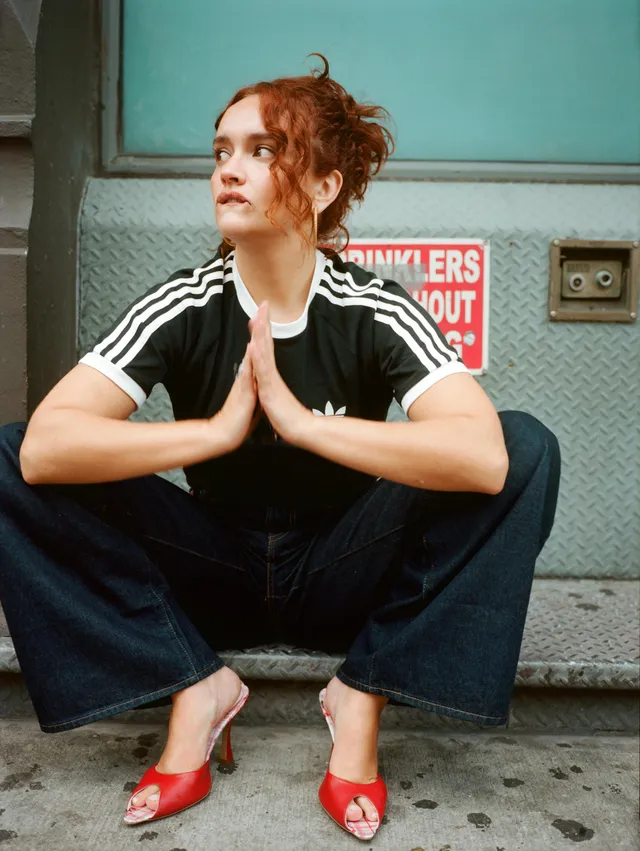 Olivia Cooke crouching in a striped shirt and red mules.