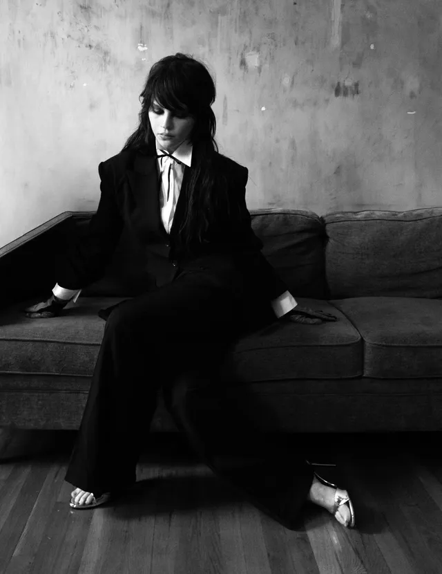Sophie Thatcher sitting in a black suit and silver heels for a monochrome portrait.