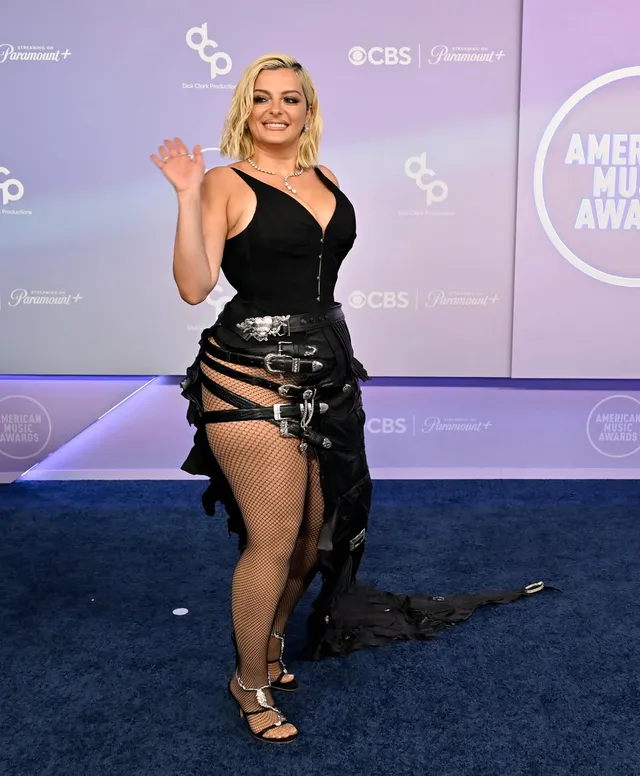 Bebe Rexha posing at an event in a black gown and metallic heels.