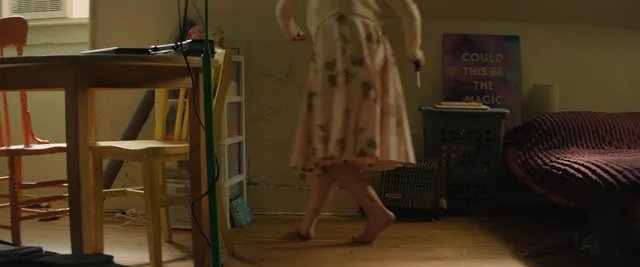 Dove Cameron walking indoors in a patterned dress and blue heels.