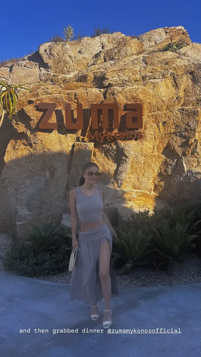 Rachel Zegler wearing a pale outfit and platform heels outside a restaurant.