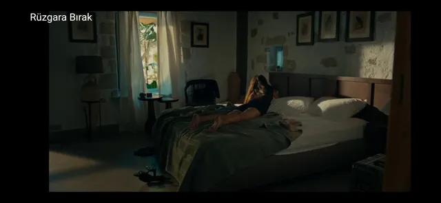 Hande Erçel reclining on a bed with bare feet visible in a scene.