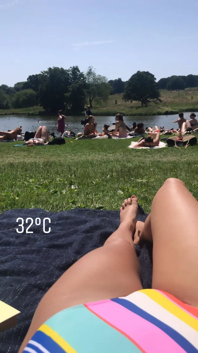 Ella Purnell relaxing on grass beside a lake.