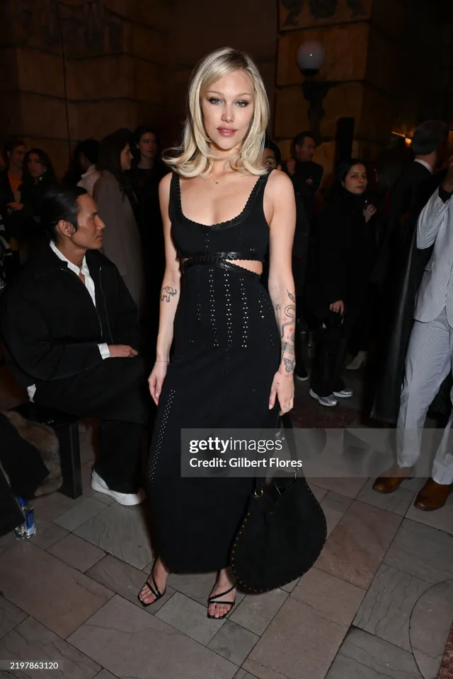 Grace VanderWaal standing at an event in a black dress and heels.