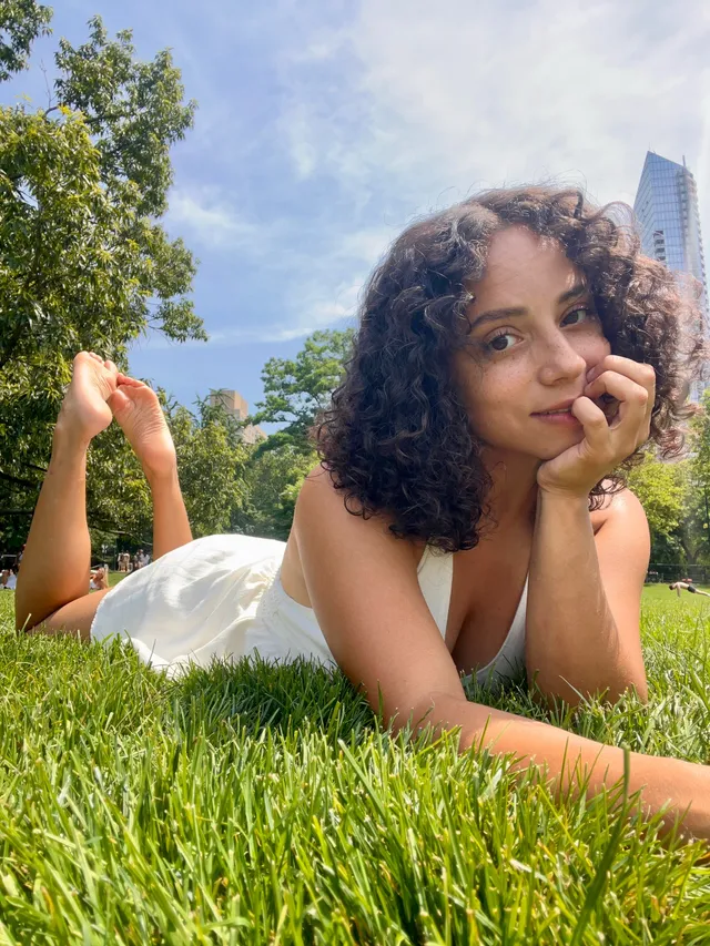 Kiana Madeira lying barefoot on grass in a pale dress.