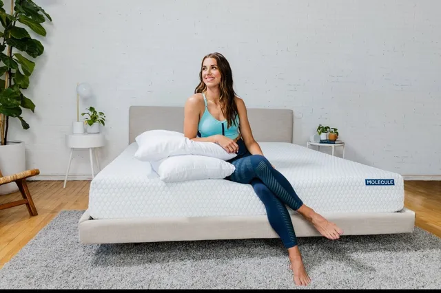 Alex Morgan sitting barefoot on the edge of a bed in a turquoise top and blue trousers.