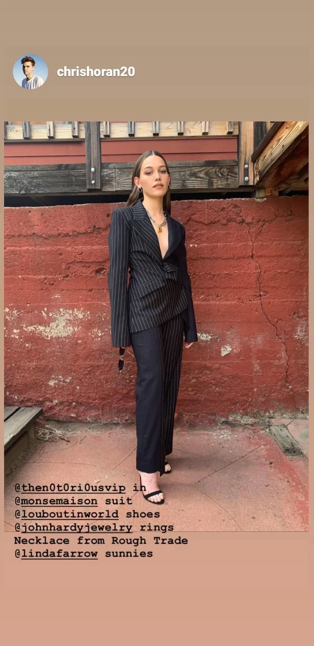 Victoria Pedretti posing outdoors in a dark suit and sandals.