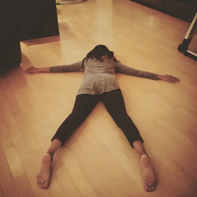 Zoe Saldaña lying on a wooden floor after stretching.