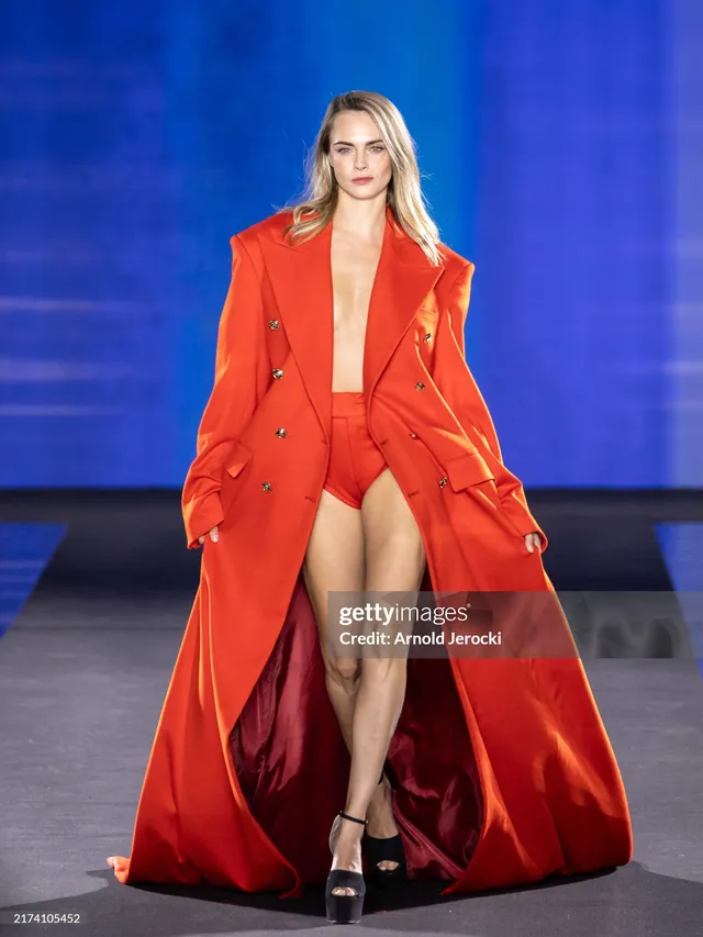 Cara Delevingne walking at a fashion event in a red coat.