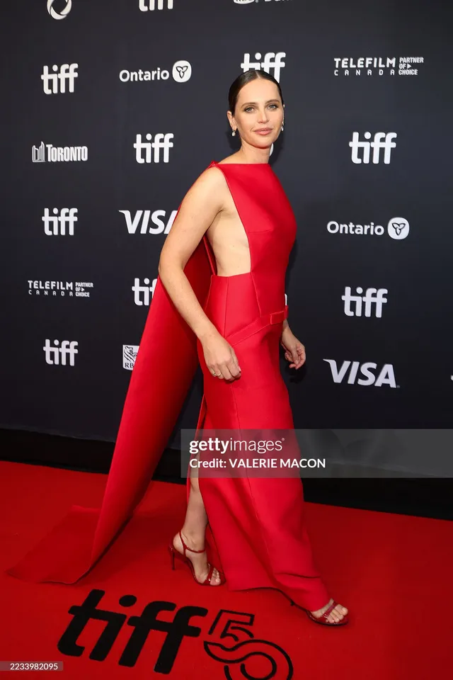 Felicity Jones posing on a film festival carpet in a red gown.