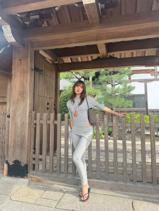 Lisa (Lalisa Manobal) standing in flat sandals and pale jeans beside a wooden garden gate.
