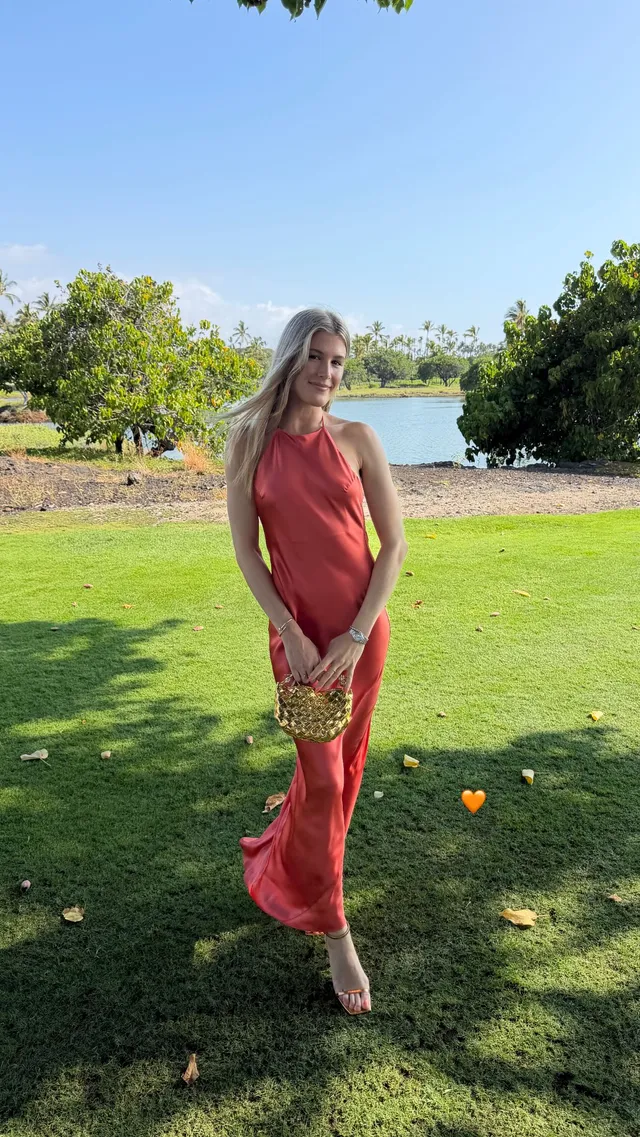 Eugenie Bouchard wearing pale heels and a flowing red dress on a garden lawn.