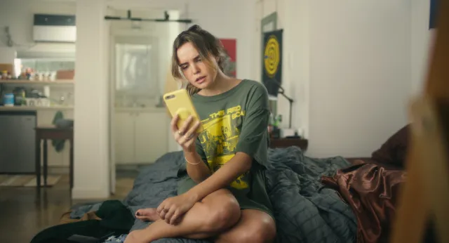 Bailee Madison sitting barefoot on a sofa in a scene.