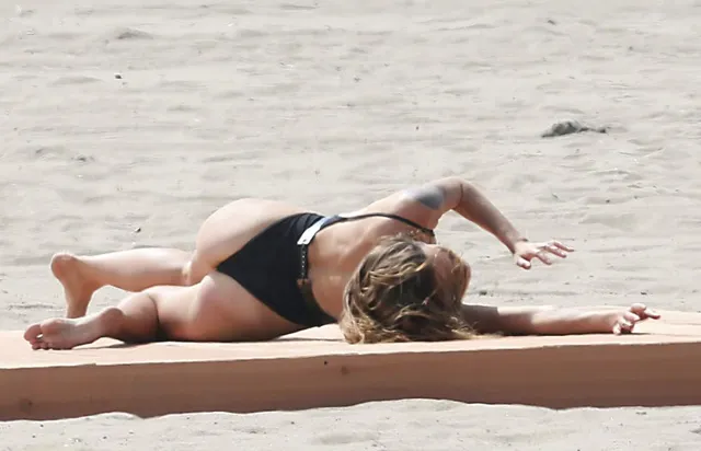 Tove Lo lying barefoot on sand in a dark swimsuit.