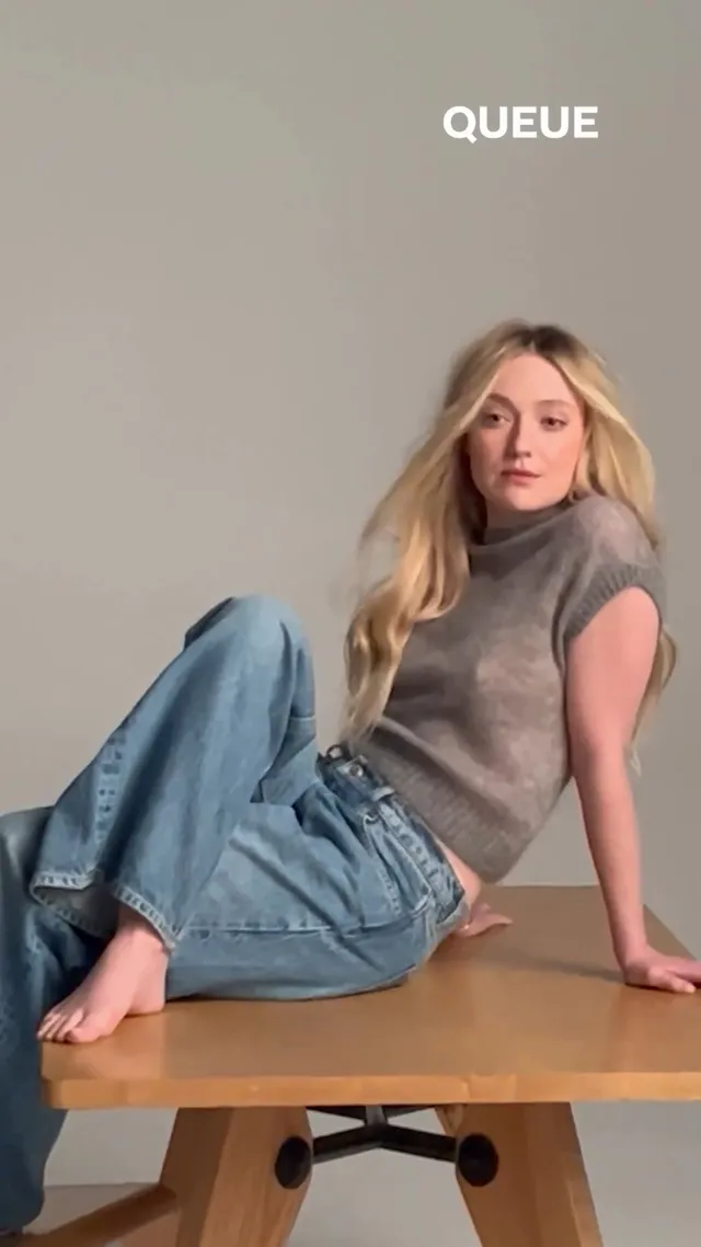 Dakota Fanning sitting barefoot in jeans and a gray top for a portrait.
