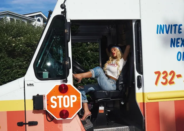 Christina Aguilera sitting in the doorway of an ice-cream van in jeans and heels.