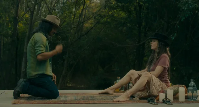 Rebecca Ferguson sitting with bare feet extended on a wooden platform among trees.