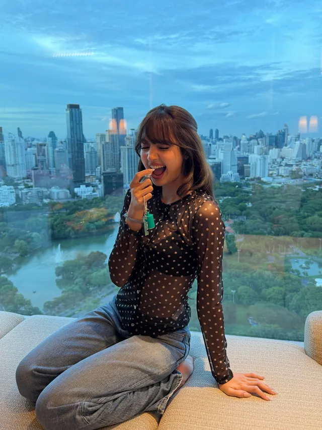 Lisa (Lalisa Manobal) sitting beside an aquarium in jeans and a patterned top.